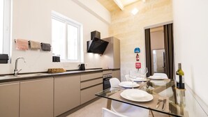 Una cocina moderna con una mesa de comedor de cristal, sillas blancas y una botella de vino.