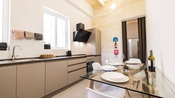 A modern kitchen with a glass dining table, white chairs, and a wine bottle.