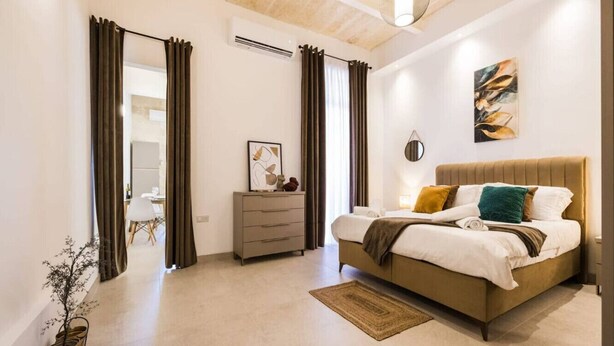 Un dormitorio moderno con una cama grande, un aparador, una mesita de noche y una planta en maceta.