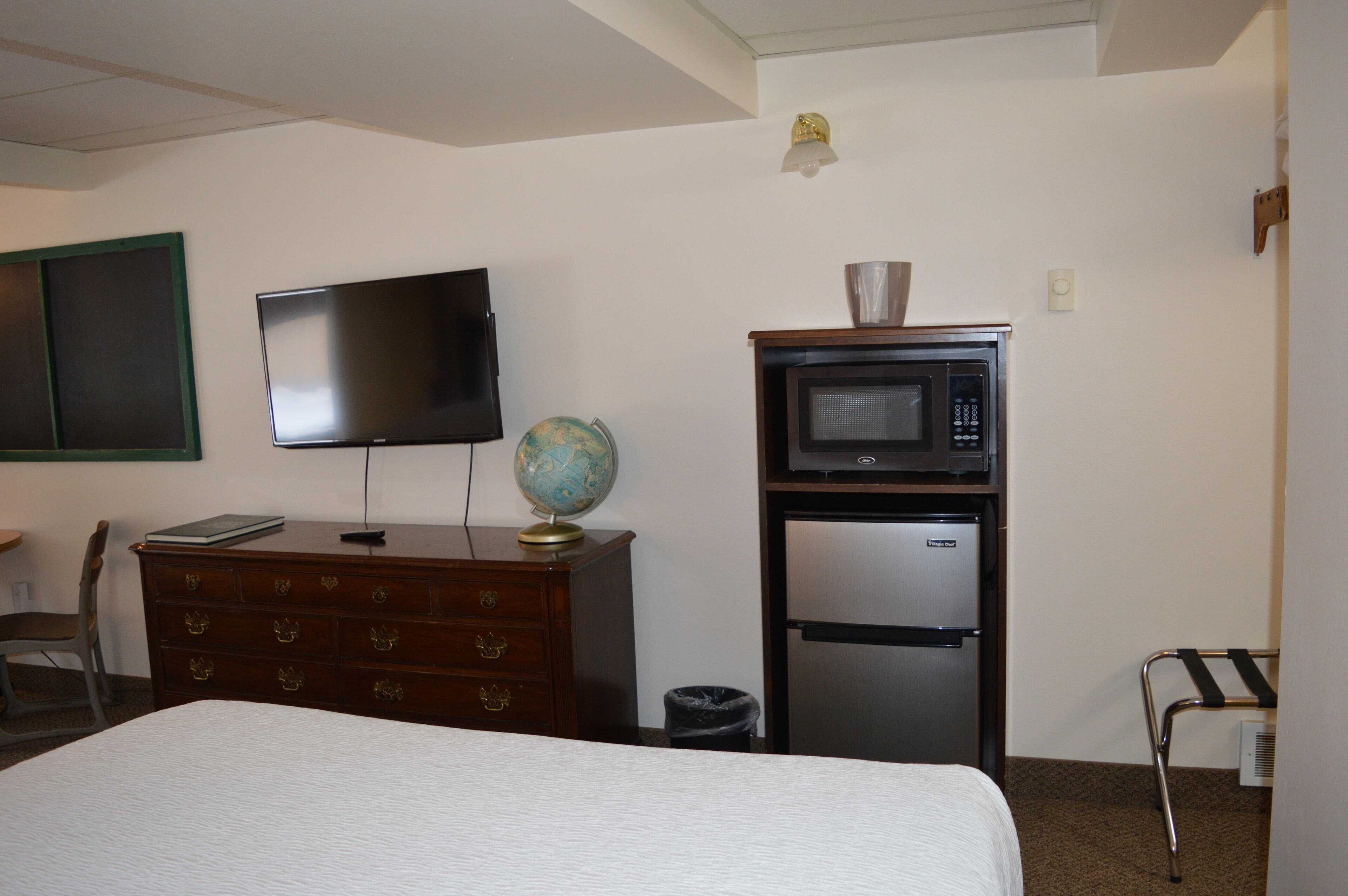 Una camera d'hotel con un letto, una cassettiera, una televisione, un forno a microonde e un mappamondo.