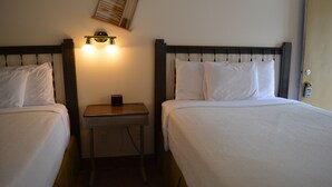 Habitación de hotel con dos camas individuales, una mesita de noche pequeña, una lámpara de pared y una puerta con cerradura.