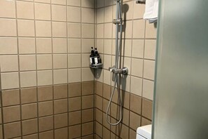 Une salle de bain carrelée de carreaux beiges, une douche avec un pommeau de douche amovible et des toilettes.