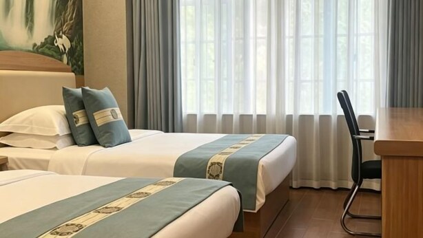 Ein Hotelzimmer mit zwei Betten, einem Schreibtisch und einem großen Fenster mit Vorhängen.