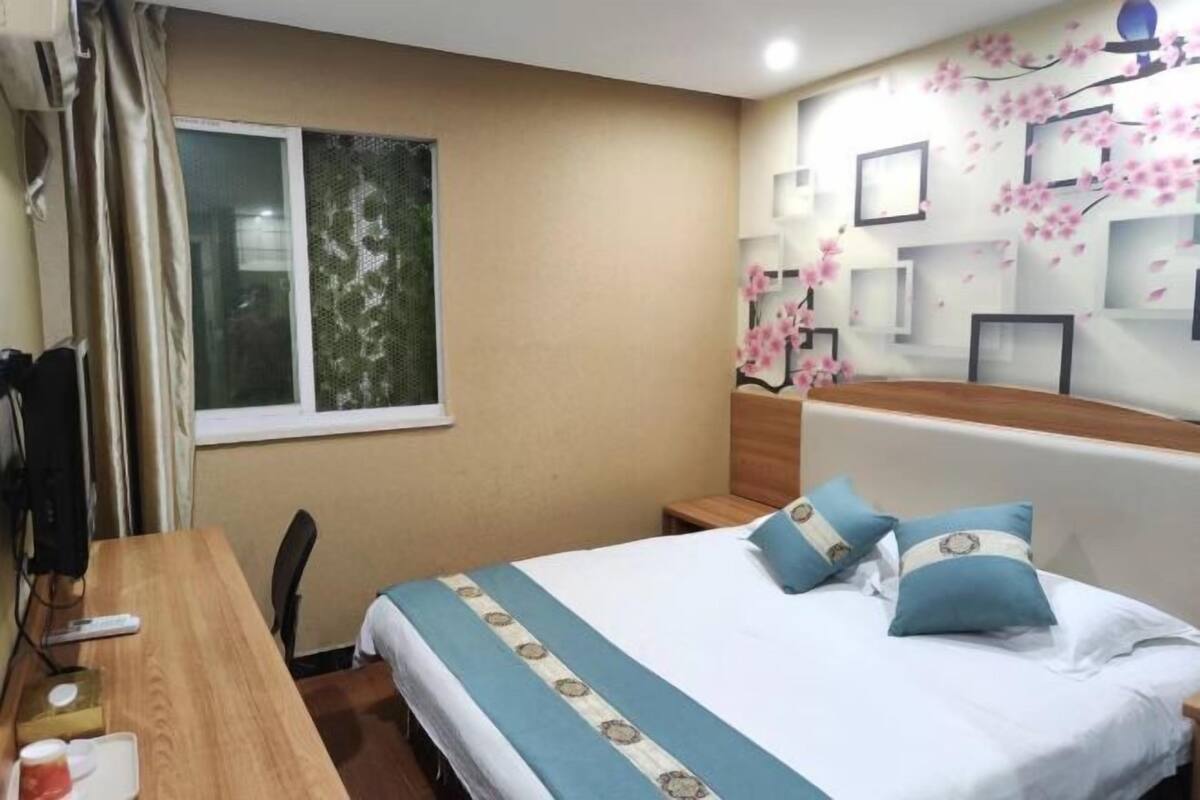 Una habitación de hotel con una cama, un escritorio de madera, una silla, una ventana y una pared decorada con cuadros enmarcados y un mural floral.