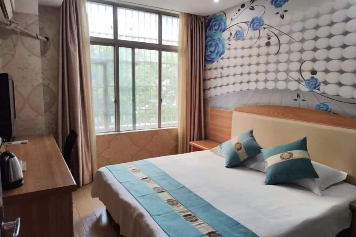 Habitación de hotel con cama, escritorio, silla, televisor y ventana con cortinas.