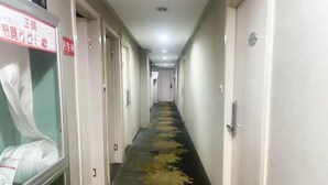 Ein Hotelgang mit Türen an beiden Seiten, einem gemusterten Teppich und einem Schild an der linken Wand.