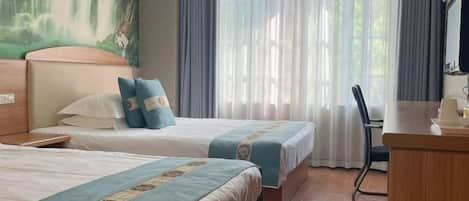 A hotel room with two beds, a desk, a chair, and a painting of a waterfall on the wall.