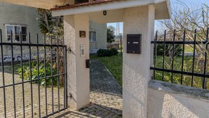 A gated entrance to a building with a tiled roof, a mailbox, and a paved pathway leading to a house with a window and a door.