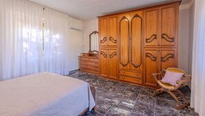 A bedroom with a bed, a wooden wardrobe, a chair, and a mirror.