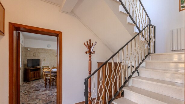 A staircase with a wooden handrail and a white balustrade, leading to a room with a tiled floor and a television in the corner.
