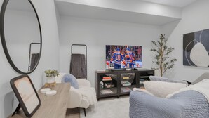 Een moderne woonkamer met een groot schilderij, een ronde spiegel, een boekenkast en een gezellige zithoek.