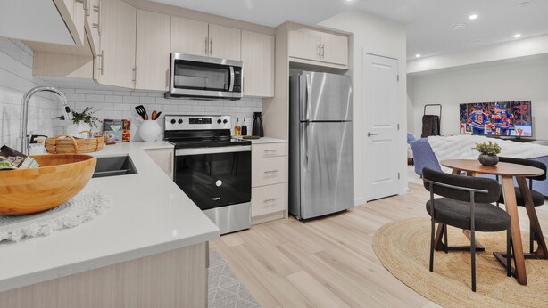 Een moderne keuken met roestvrijstalen apparatuur, een houten kom op het aanrecht en een eethoek met een tafel en stoelen.