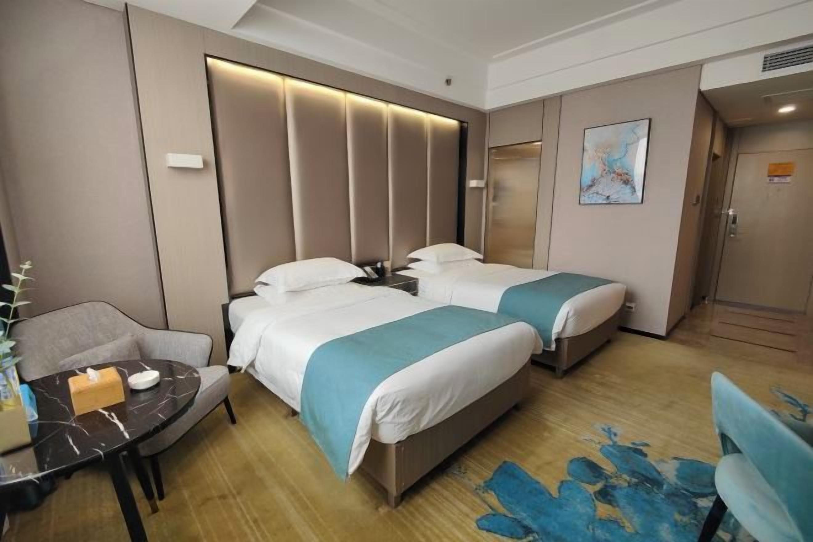 A hotel room with two beds, a desk, a chair, and a painting on the wall.
