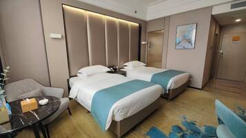 A hotel room with two beds, a desk, a chair, and a painting on the wall.