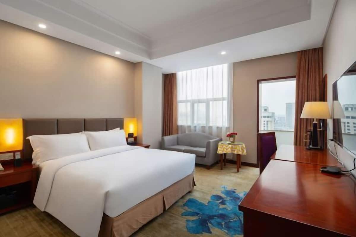 Habitación de hotel con cama, escritorio, silla, una mesita y televisor.
