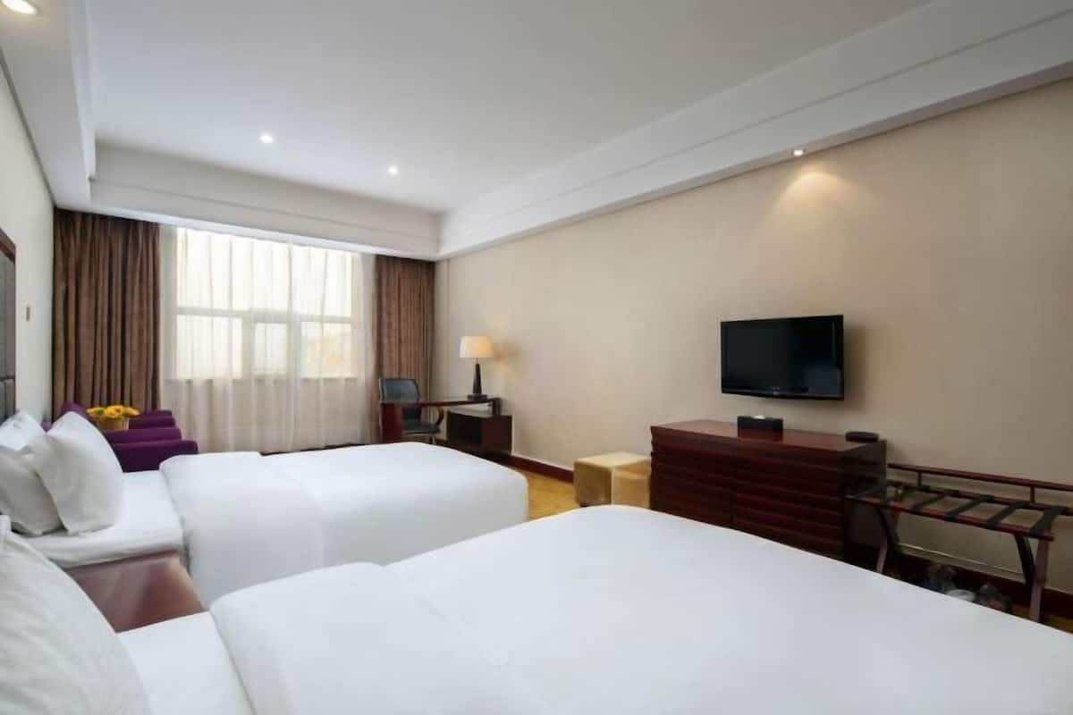 Habitación de hotel con dos camas, televisor, escritorio y ventana con cortinas.