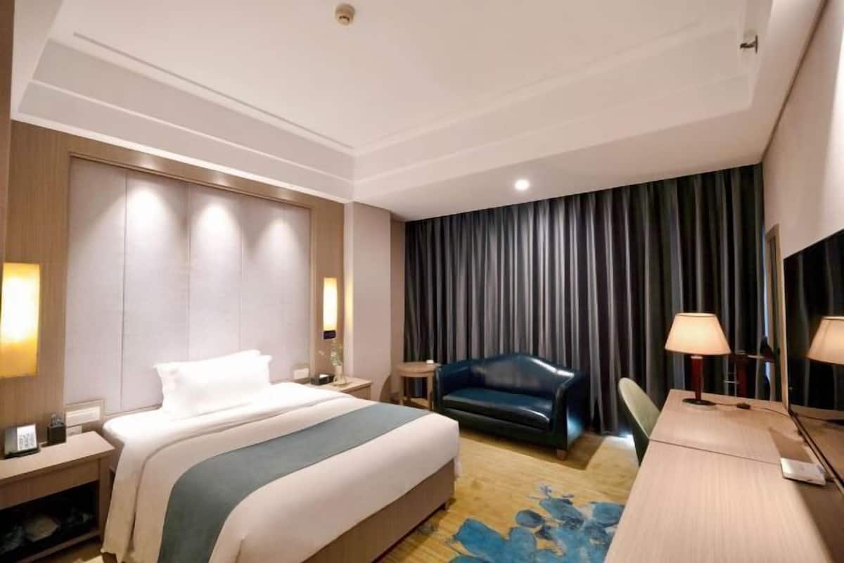 Una habitación de hotel con cama, escritorio, silla, lámpara y cortina.