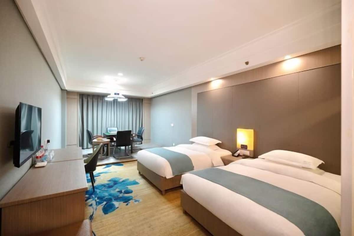 Habitación de hotel con dos camas, un escritorio, un televisor y una lámpara de escritorio.