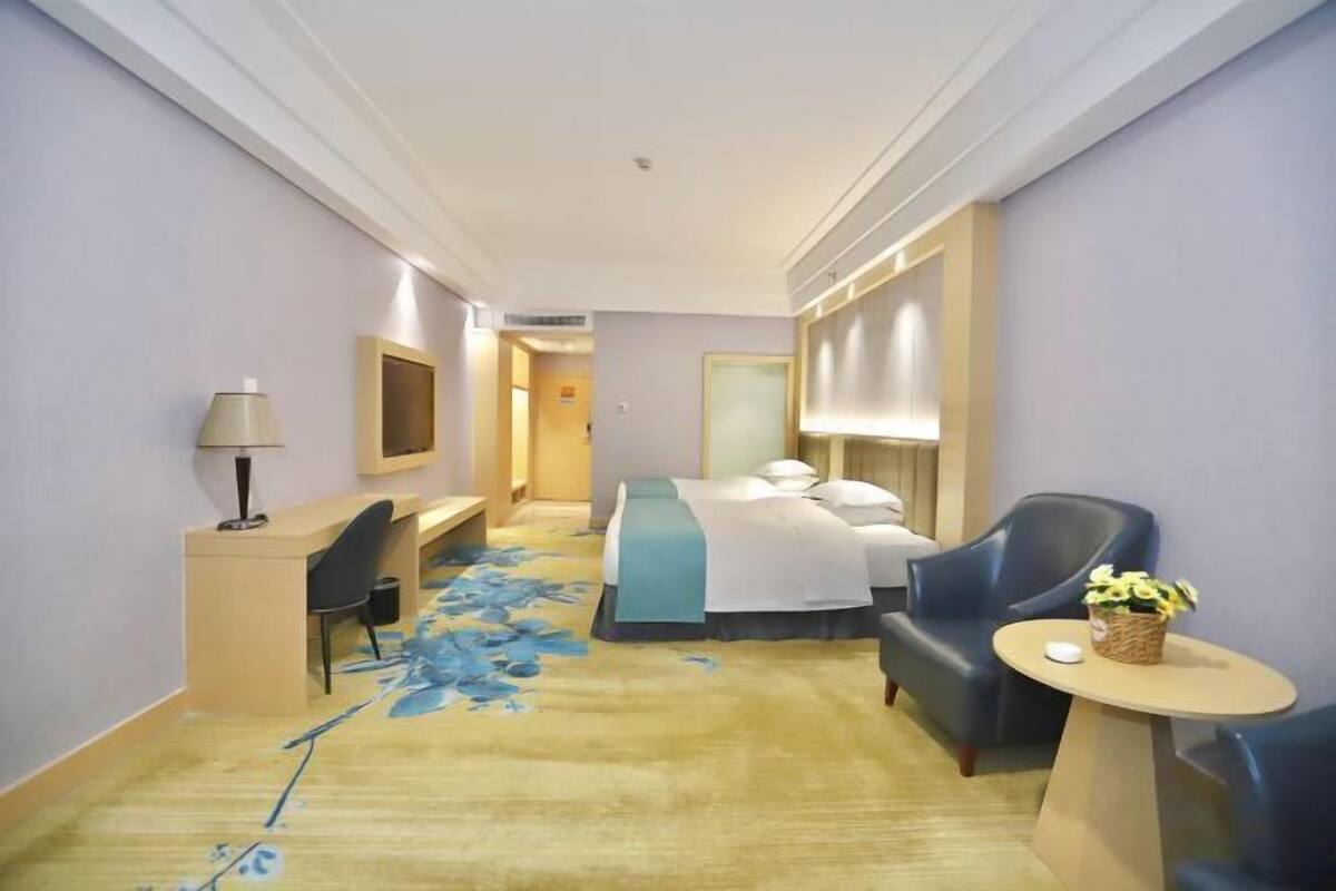 Habitación de hotel con cama, escritorio, silla, una mesita con una cesta y alfombra de estampado floral azul.