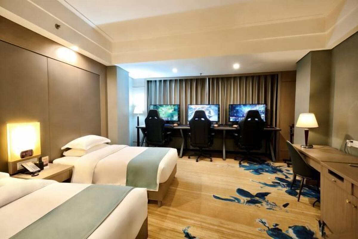 Habitación de hotel con dos camas, un escritorio con dos monitores y piso de madera con un diseño azul.