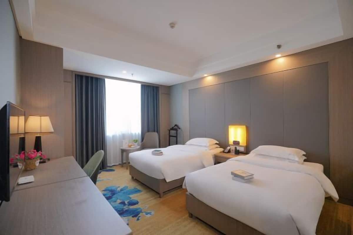 Habitación de hotel con dos camas, un escritorio, una silla, un televisor y una ventana con cortinas.