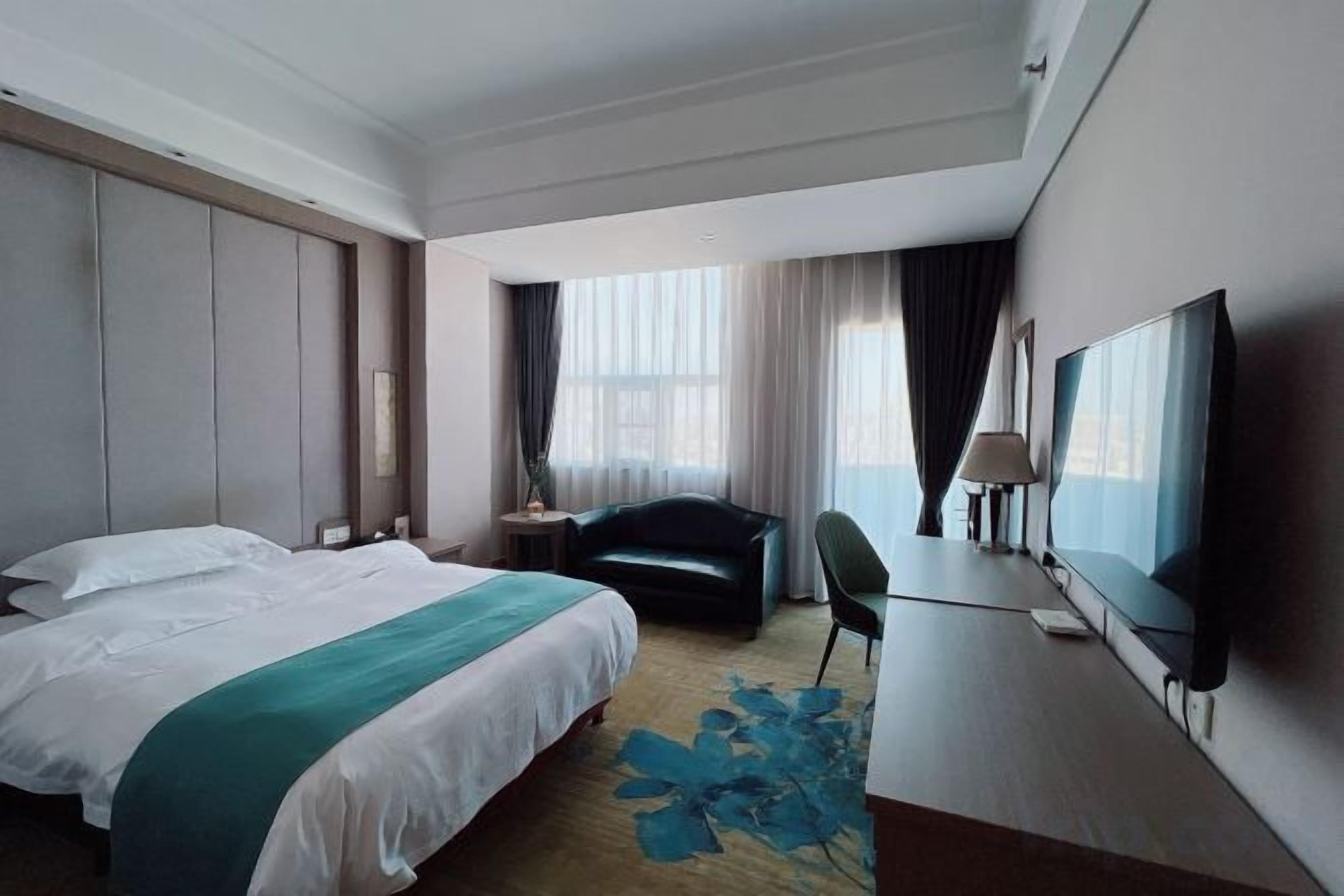 Habitación de hotel con una cama grande, un escritorio, una silla, un televisor y una ventana con cortinas.