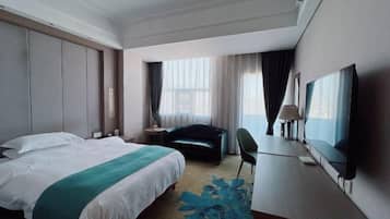 Habitación de hotel con una cama grande, un escritorio, una silla, un televisor y una ventana con cortinas.