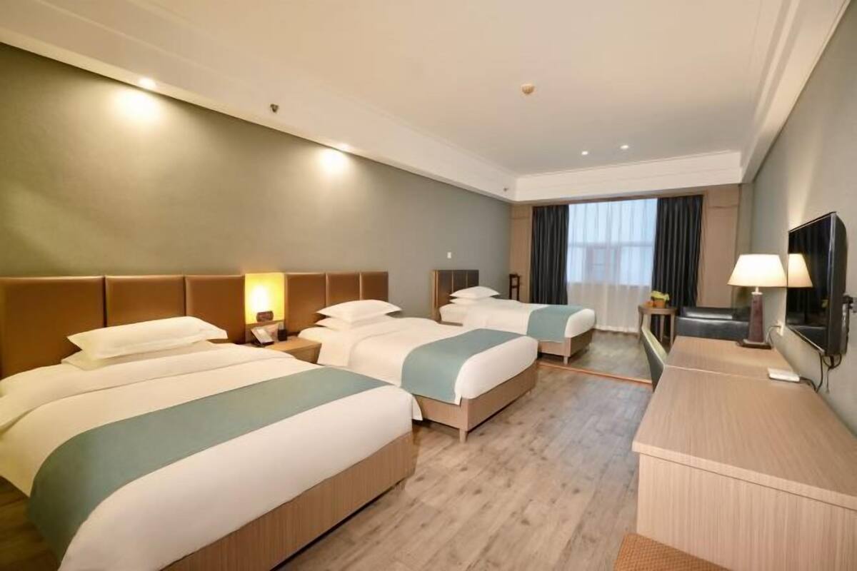 Habitación de hotel con tres camas, un escritorio, una silla y un televisor.