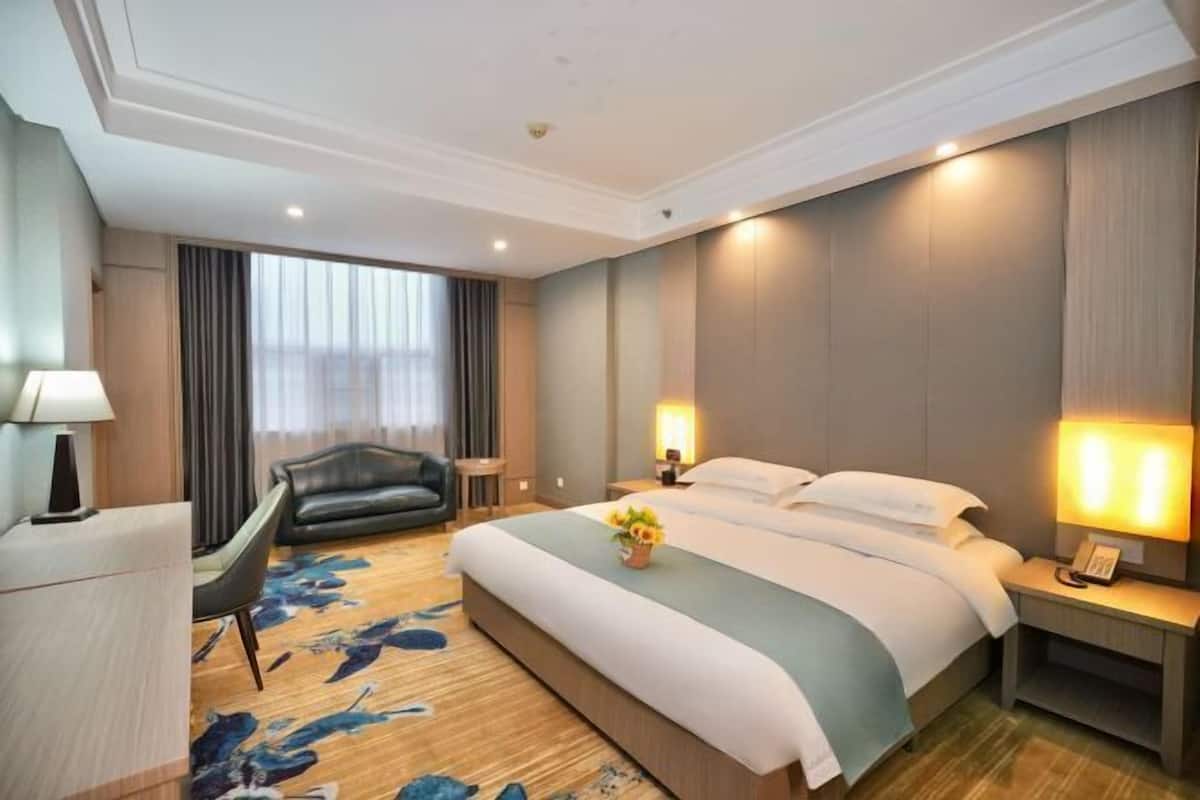 Habitación de hotel con una cama grande, un escritorio, una silla y una mesita de noche con lámpara.