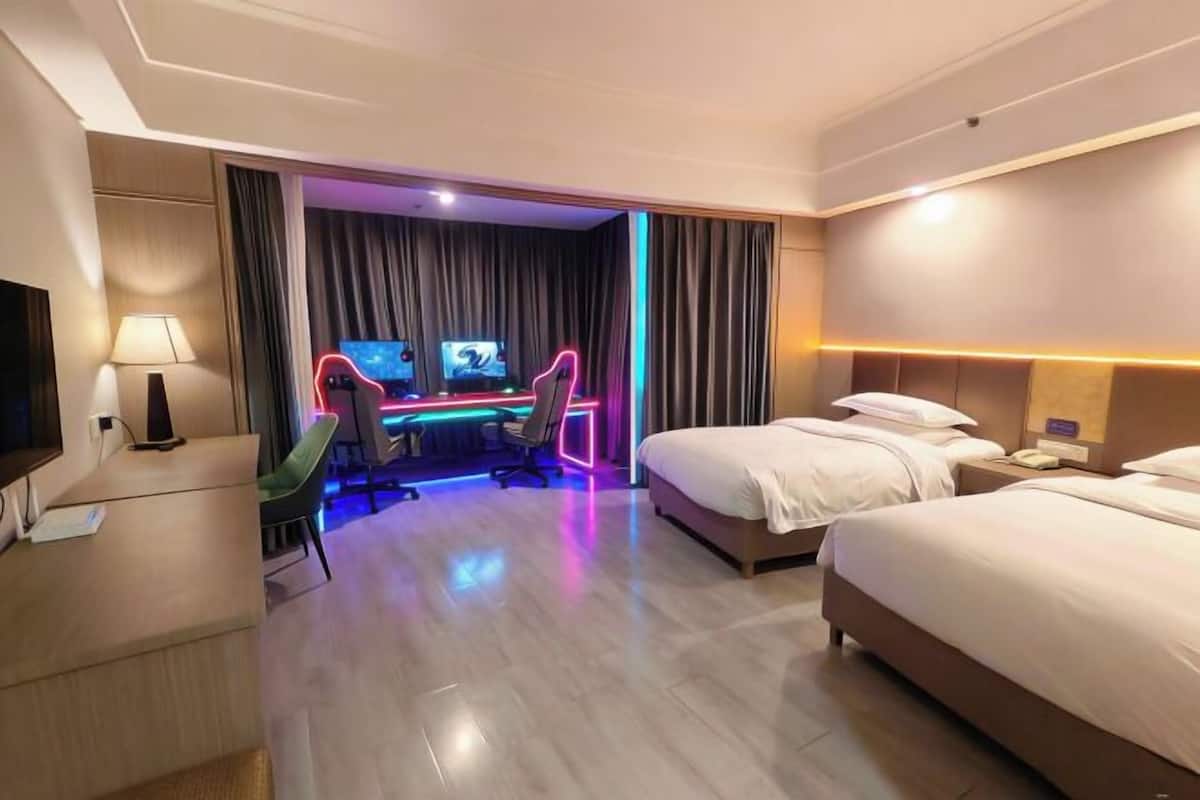 Habitación de hotel con dos camas, un escritorio con computadora, televisor y un letrero de neón.