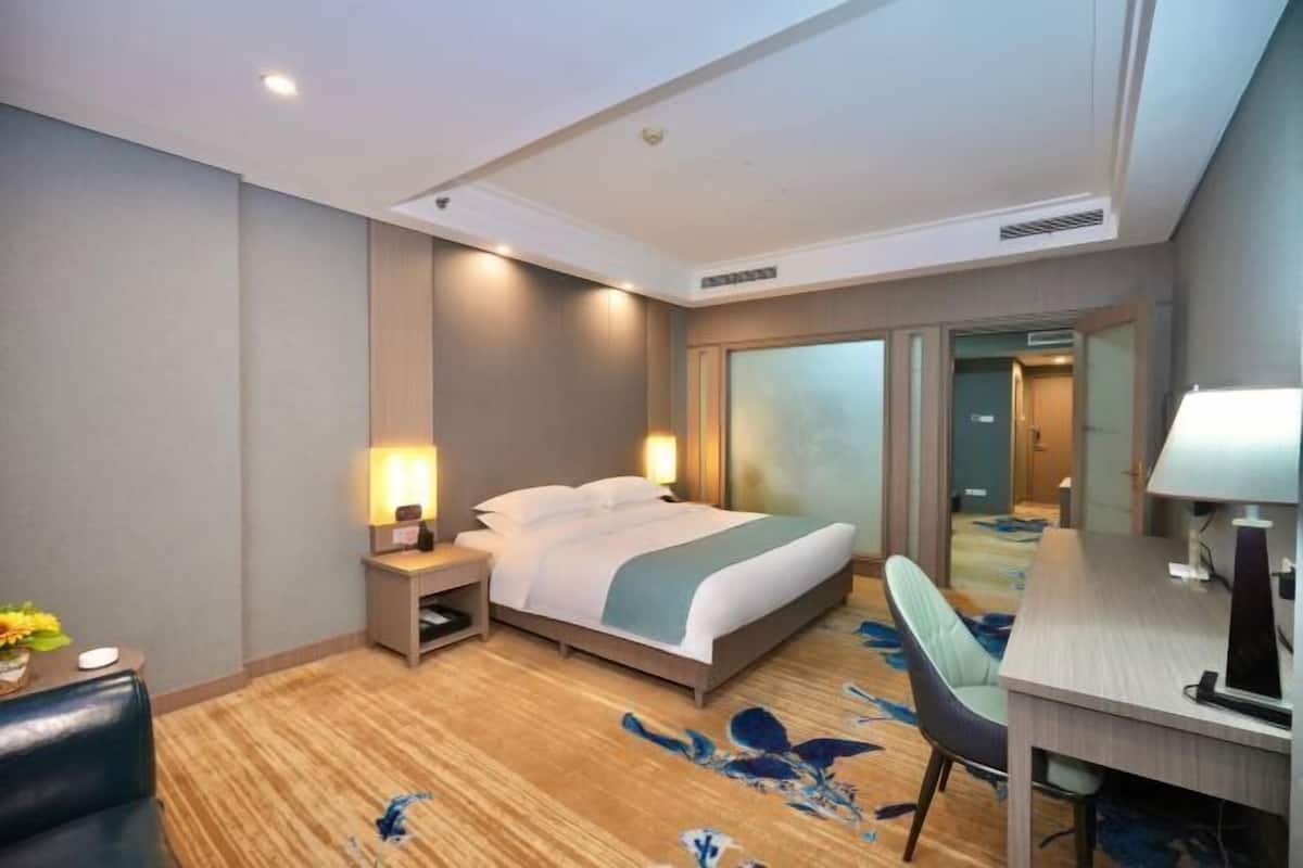 Habitación de hotel con cama, mesita de noche, lámpara, escritorio, silla y alfombra con estampado floral.