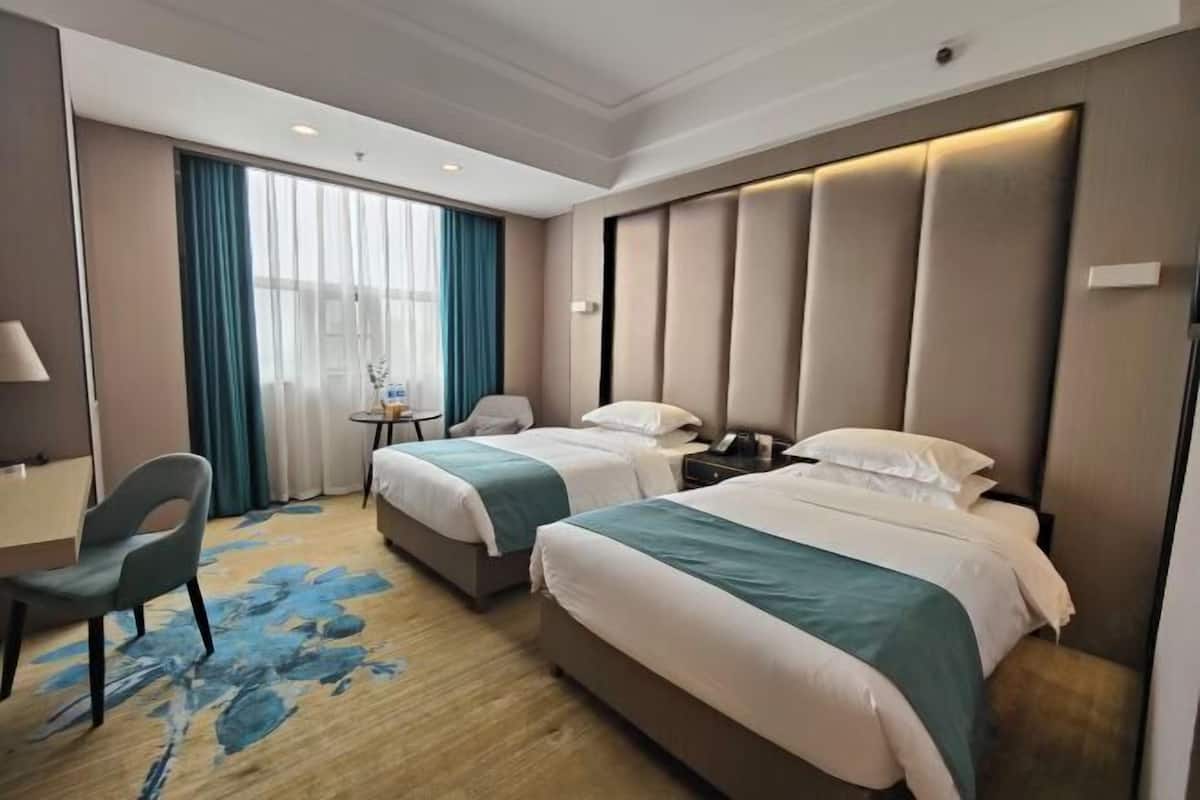Habitación de hotel con dos camas, un escritorio, una silla y una mesita de noche con lámpara.