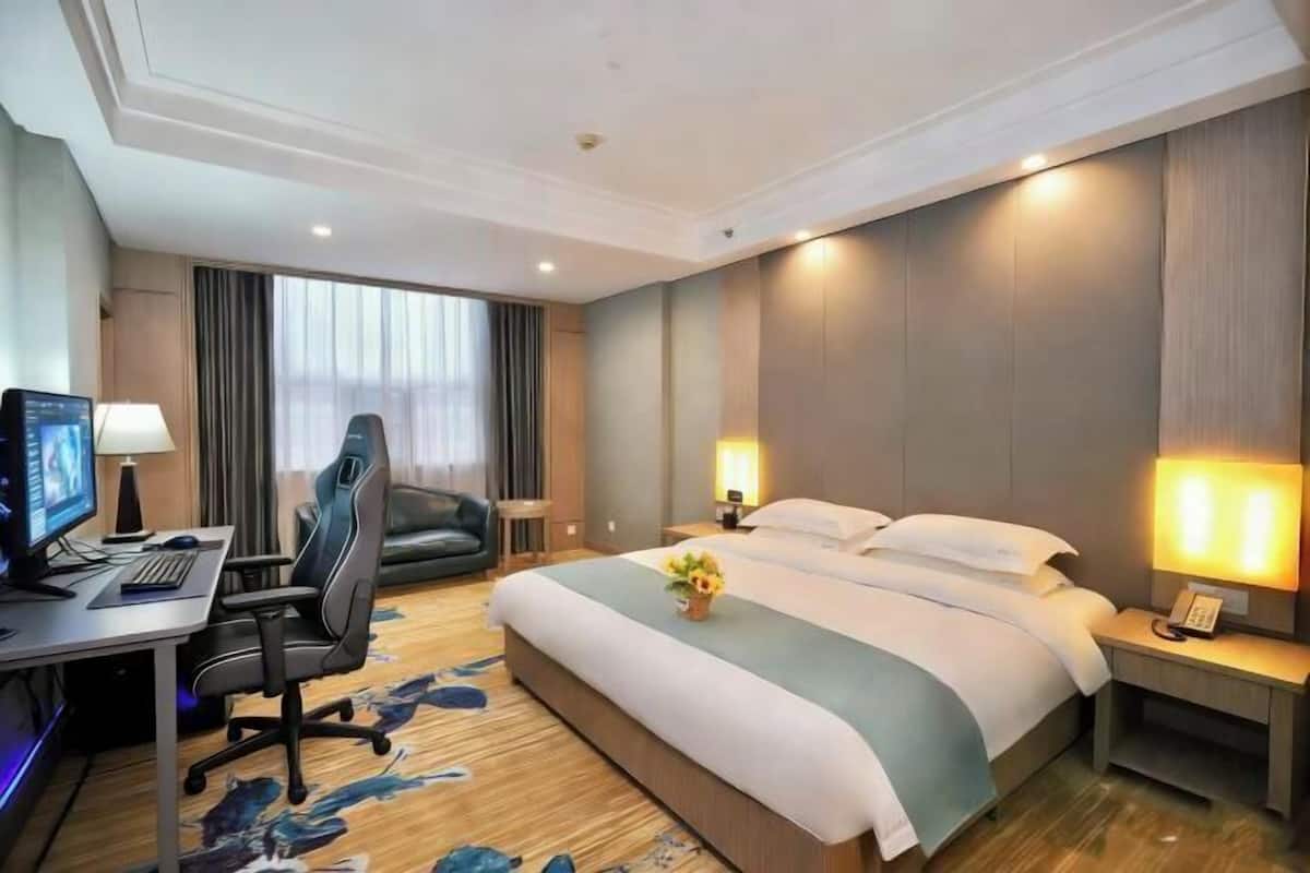 Una habitación de hotel con cama, escritorio, computadora, silla y lámparas.
