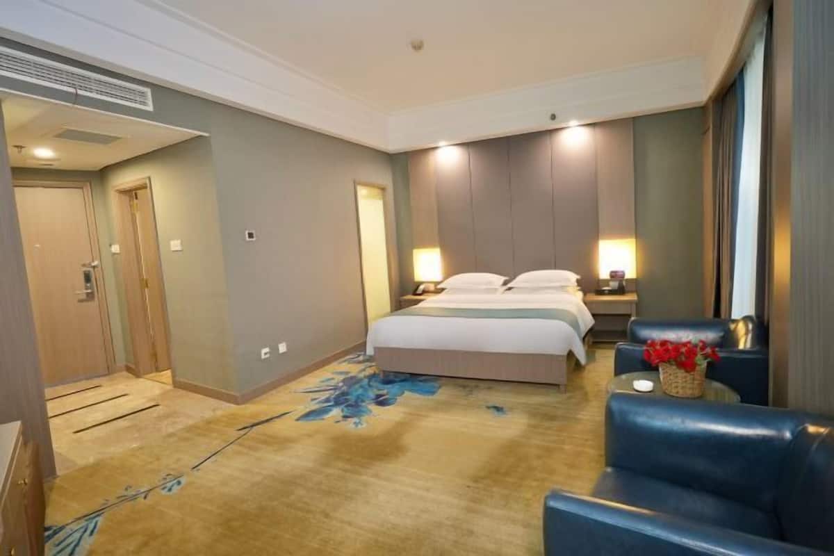 Una habitación de hotel con una cama, mesitas de noche, una silla, una mesita con un florero y una puerta.