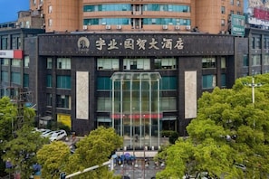 A modern building with a large glass entrance, surrounded by trees and other buildings. - Guomao Hotel (Yueyang)