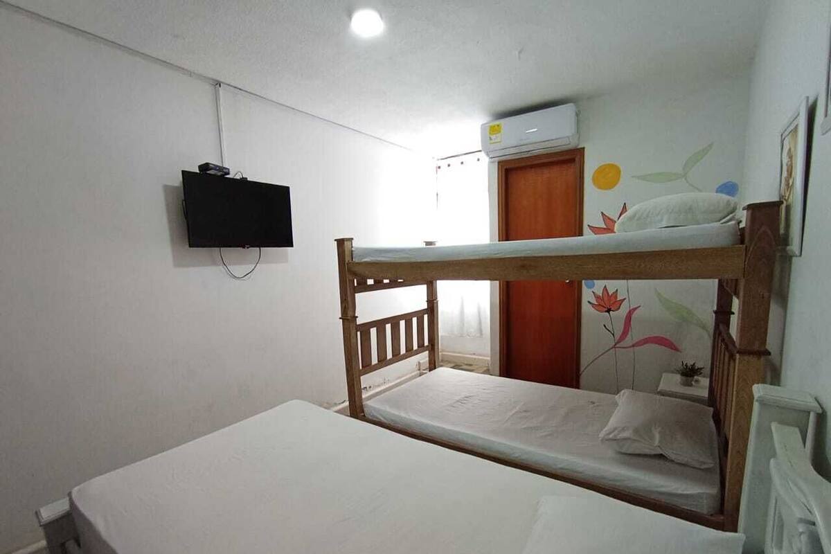 Una habitación individual con una cama litera, una cama individual, un televisor montado en la pared y una ventana con cortinas.