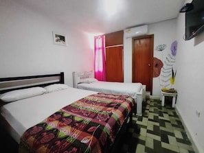 A room with two single beds, a patterned bedspread, a small table with a vase, a wall-mounted TV, and a checkered floor. - HOTEL HABIBI (Barranquilla)