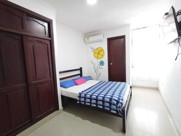A bedroom with a bed, a wardrobe, an air conditioning unit, and a door. - HOTEL HABIBI (Barranquilla)