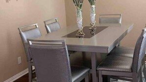 Comedor con una mesa rectangular, seis sillas, dos jarrones con flores y arte abstracto en la pared.