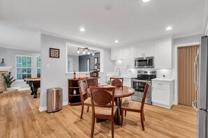 Una cocina moderna con armarios blancos, electrodomésticos de acero inoxidable y un comedor con sillas de madera.