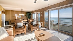 A spacious living area with a large sliding glass door leading to a balcony with a view of the ocean. There is a ceiling fan, a dining table, and several chairs. - Oceanfront Getaway | Ocean Views, Fire Pit, BBQ, Beach Access (Carlsbad)