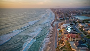 Vista aérea de un pueblo costero con playa, edificios residenciales y cielo despejado.