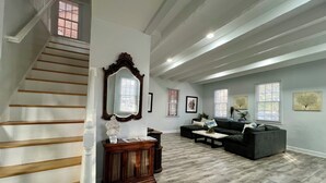 Un salon spacieux avec un escalier, un grand miroir et un canapé de couleur sombre.