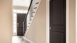 Un couloir avec un escalier, une porte sombre et un mur de couleur claire.
