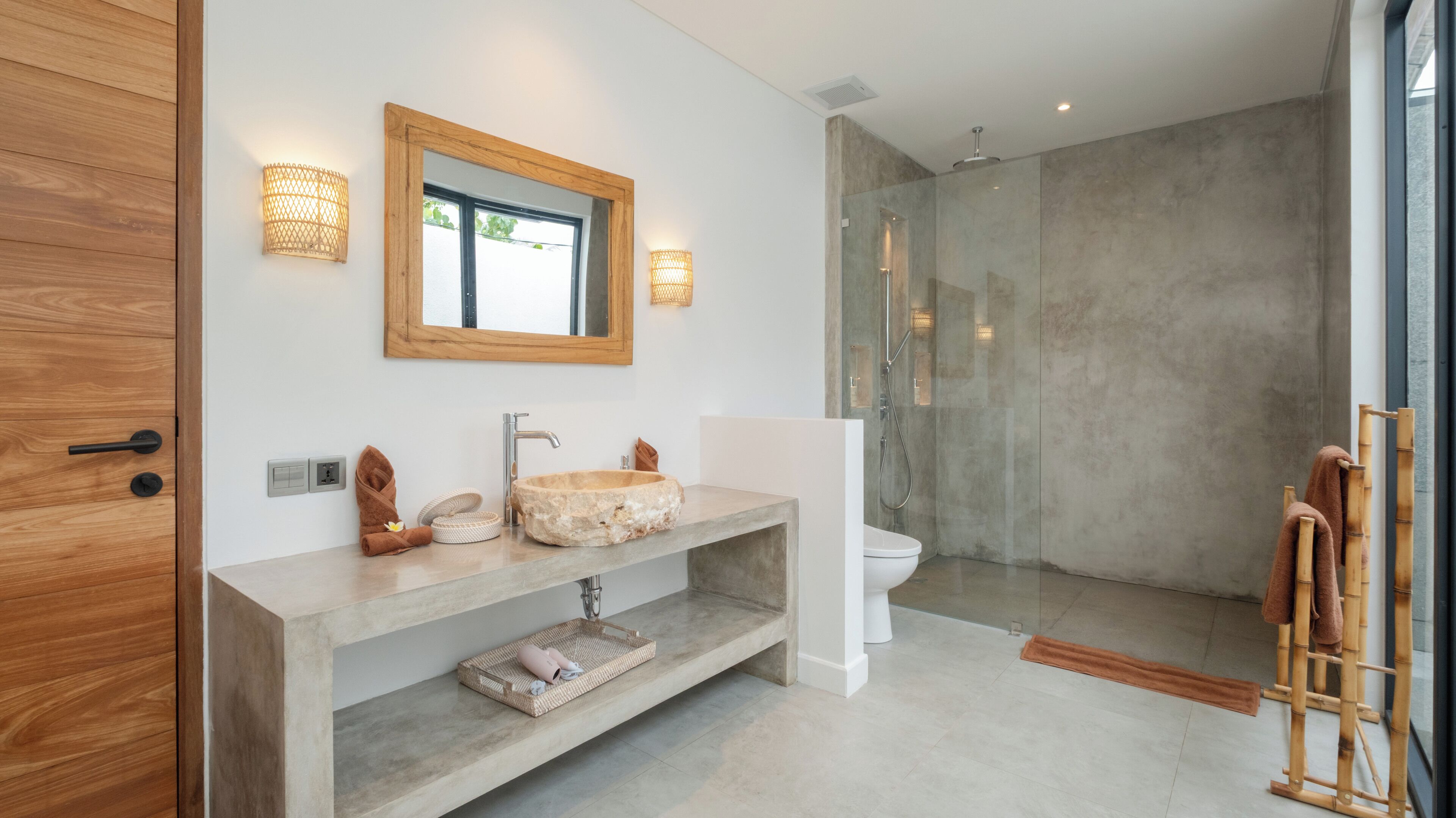 Ein modernes Badezimmer mit Waschtisch aus Holz, einem Steintonne und einer Glasdusche sowie einem Spiegel.
