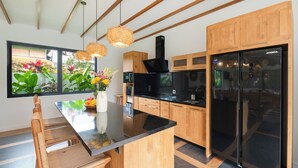 Een moderne keuken met houten kasten, een zwarte koelkast en een eethoek met een glazen tafel en stoelen.