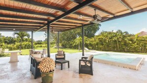 An outdoor covered patio with wicker furniture, a pool, and a view of palm trees. - Private 3BR Villa with Pool, BBQ & Spacious Garden (Punta Cana)