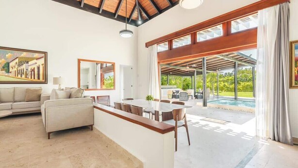 A spacious living area with a large dining table, a sofa, and a view of a swimming pool. - Private 3BR Villa with Pool, BBQ & Spacious Garden (Punta Cana)