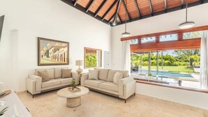 A spacious living room with two sofas, a coffee table, and a large window offering a view of a swimming pool and greenery. - Private 3BR Villa with Pool, BBQ & Spacious Garden (Punta Cana)