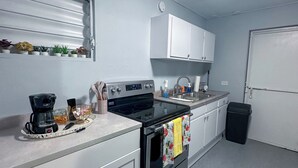 A compact kitchen with white cabinets, a stove, a coffee maker, and a trash bin.